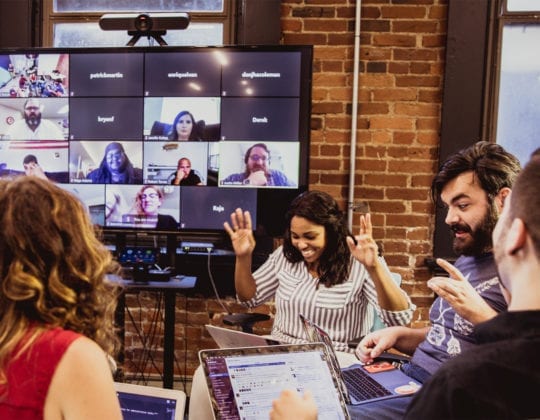 Kenzie Academy Students working in-person on our downtown Indianapolis campus with remote students who are tuning in via Zoom video chat on a large TV screen.