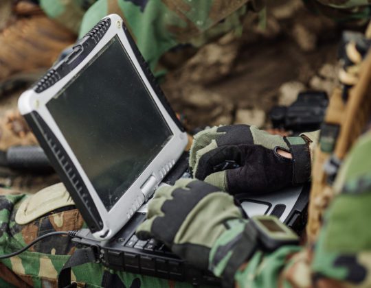 Military member holding a laptop out in the field