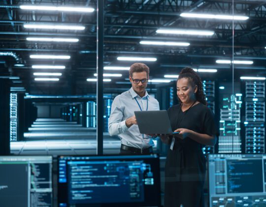 Male and female SOC Analysts working in Cybersecurity on a laptop with a server room in the background.